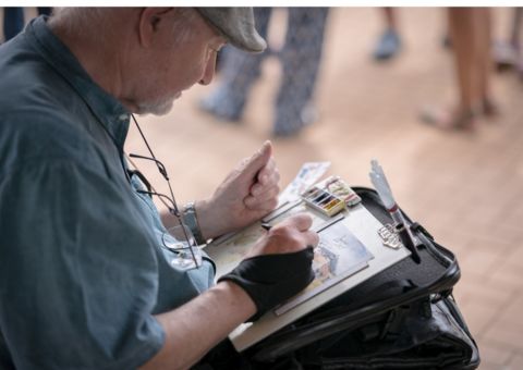 Ein Mann sitzt in der Hocke und zeichnet etwas auf ein Blatt Papier