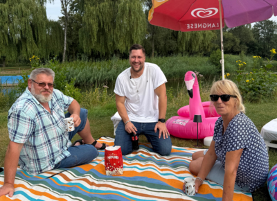 Rene Böhm zusammen mit den Betreibern des Naturfreibads auf einer Picknickdecke mit Popcorn
