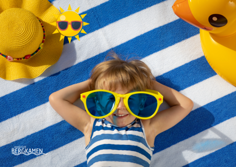 Kind liegt mit Sonnerbrille auf einem Handtuch