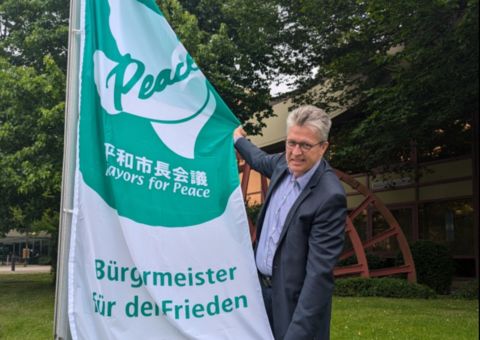 Bernd Schäfer mit der Flagge der Mayors for Peace for dem Rathaus
