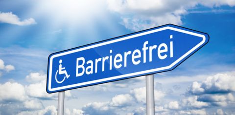 Blauer Wegweiser mit Rollstuhlsymbol und dem Schriftzug 'Barrierefrei' vor wolkigem Himmel
